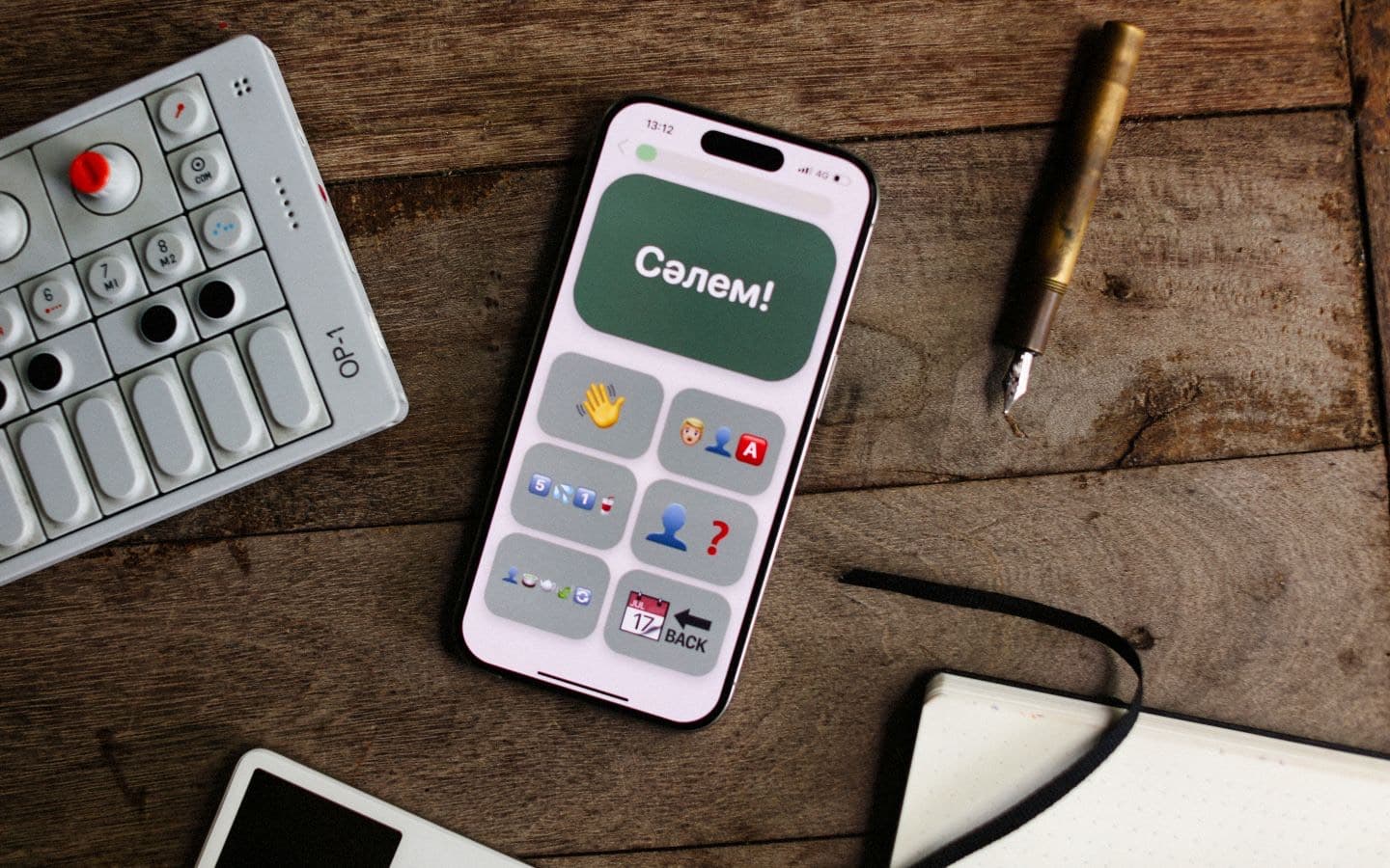 Smartphone mit geöffneter App neben einem Synthesizer, Stift und Notizbuch auf Holz