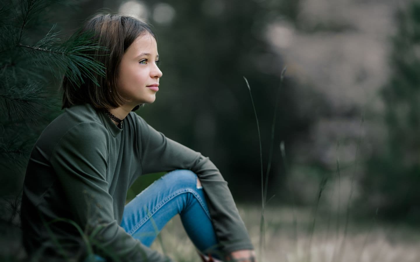 Mädchen in Freizeitkleidung sitzt im Sommer auf einer grünen Wiese und blickt verträumt in die Ferne
