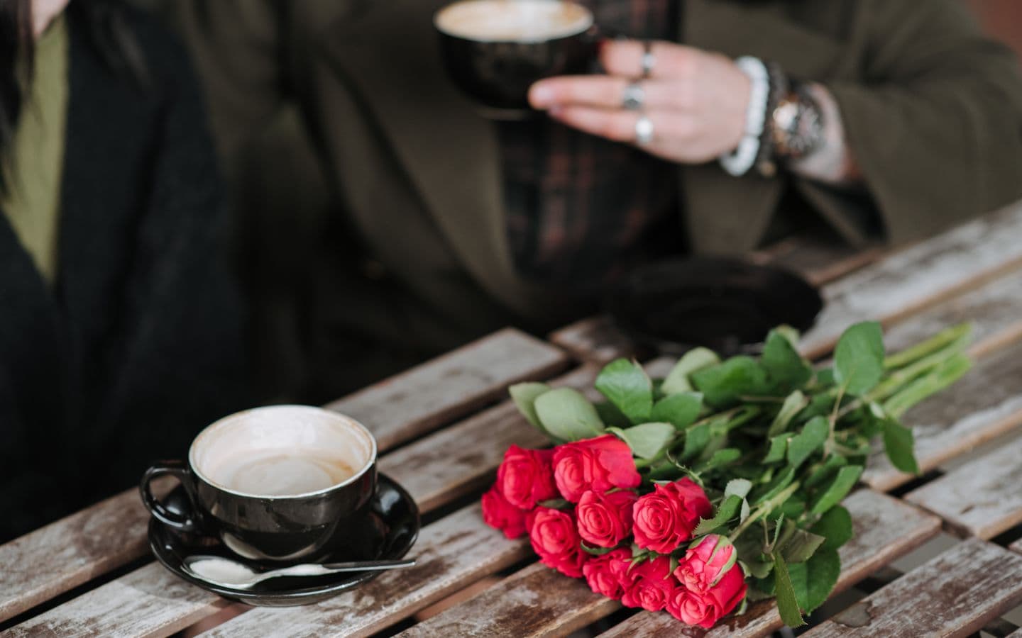 Mann mit Cappuccino sitzt mit seiner Freundin an einem Holztisch mit Blumenstrauß