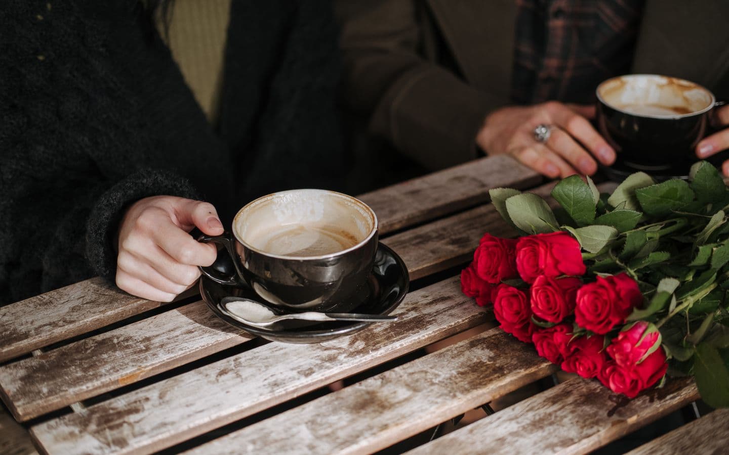 Paar mit Kaffeetassen an einem Holztisch mit roten Rosen, von oben fotografiert
