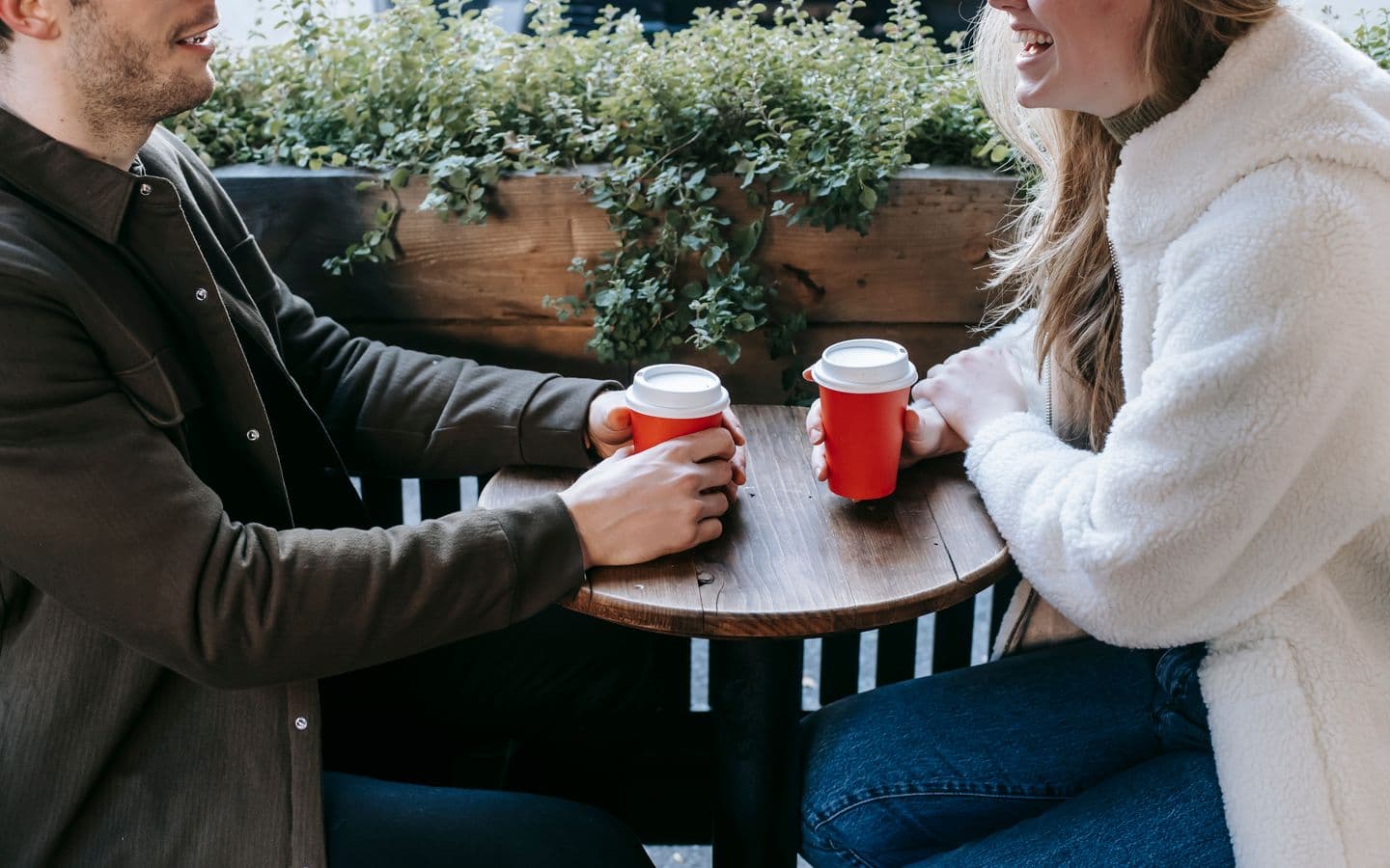 Paar sitzt bei einem Date mit Kaffee in Pappbechern an einem Holztisch und schaut sich an