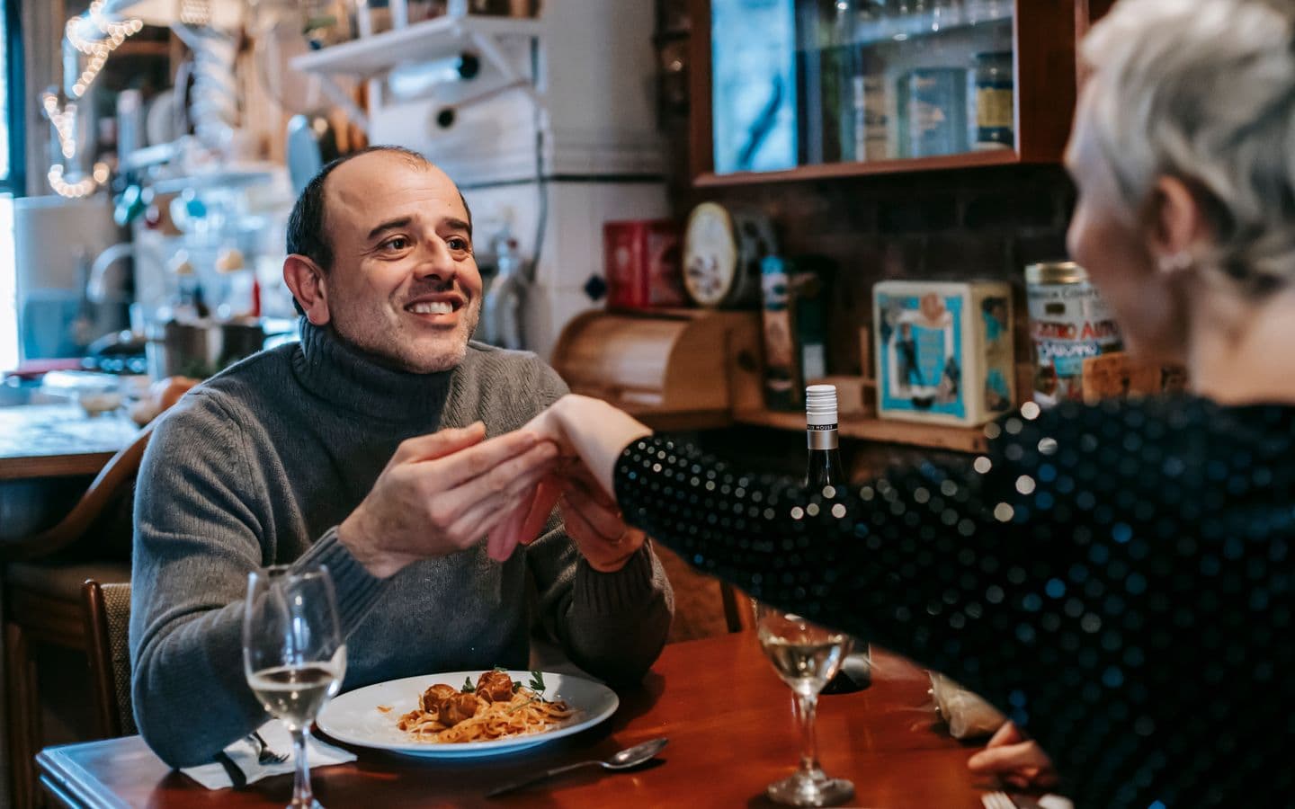 Glücklicher Mann in Freizeitkleidung hält beim romantischen Abendessen im Restaurant die Hand seiner Freundin