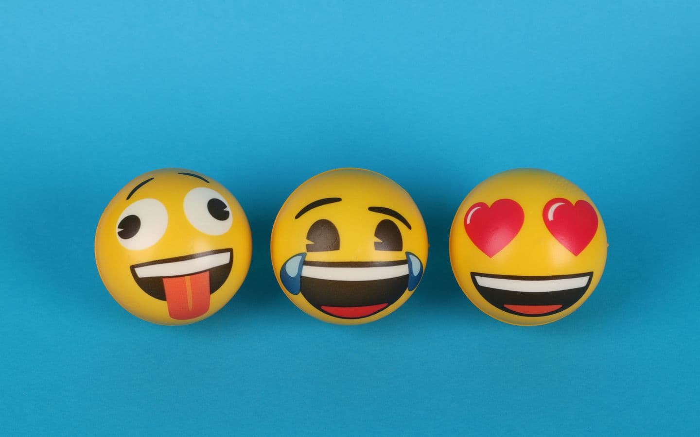 Drei verspielte Emoji-Bälle mit unterschiedlichen Gesichtsausdrücken auf blauem Hintergrund