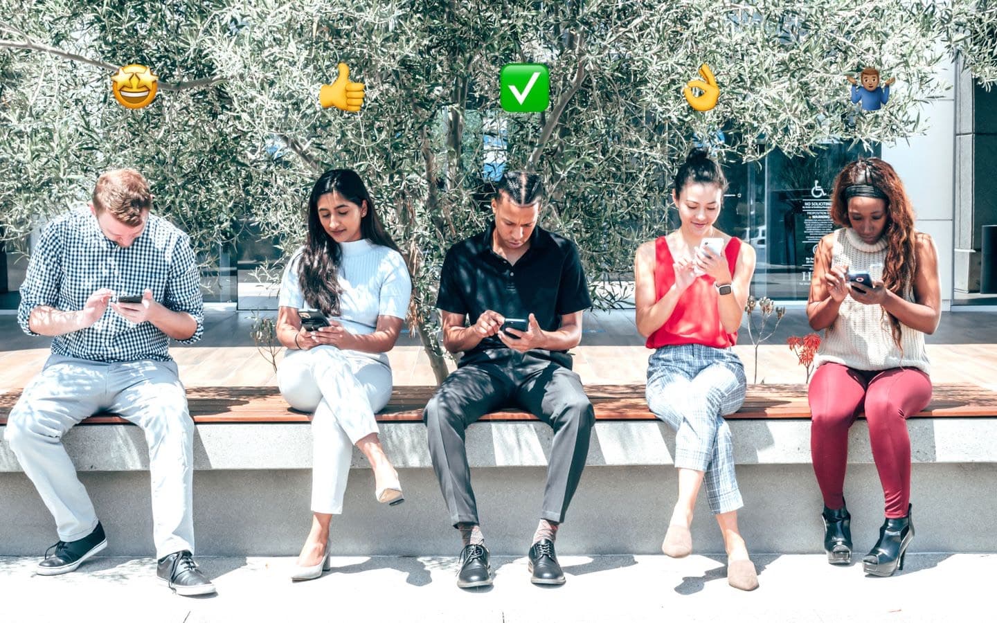 Gemischte Gruppe sitzt im Freien und schaut auf Smartphones, darüber schweben Emojis