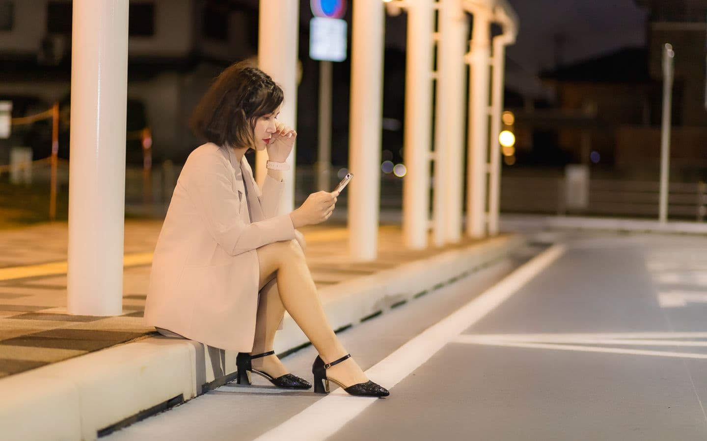 Frau sitzt nachts auf einem Gehweg und nutzt im Licht der Stadt ihr Smartphone