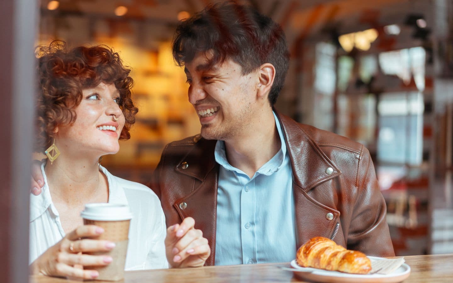 Paar lacht und genießt Kaffee und Croissant in einem gemütlichen Café