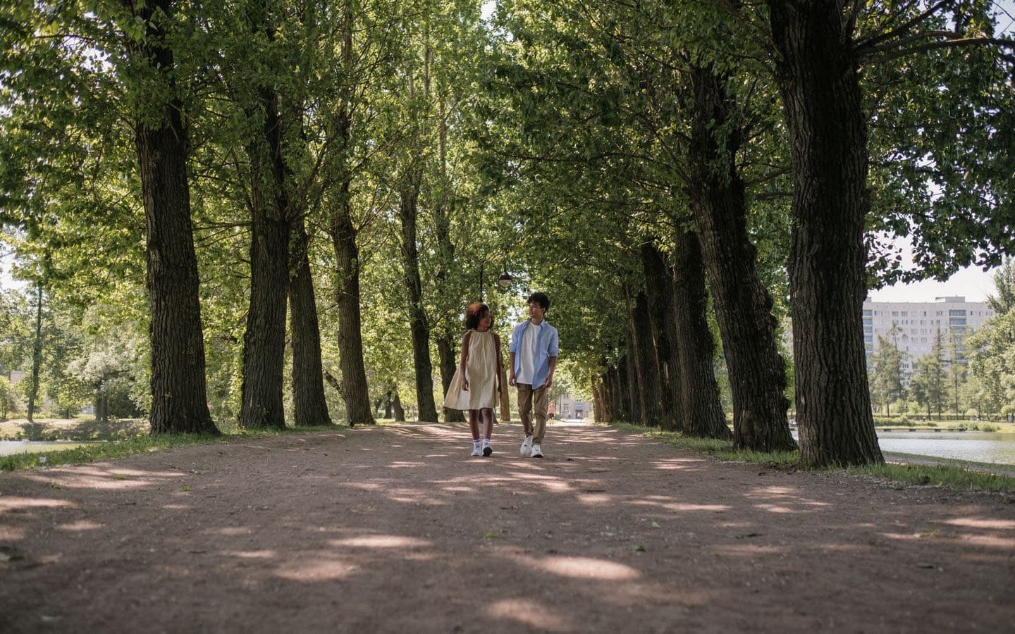 Junges Paar spaziert an einem sonnigen Tag unter Bäumen durch einen Park