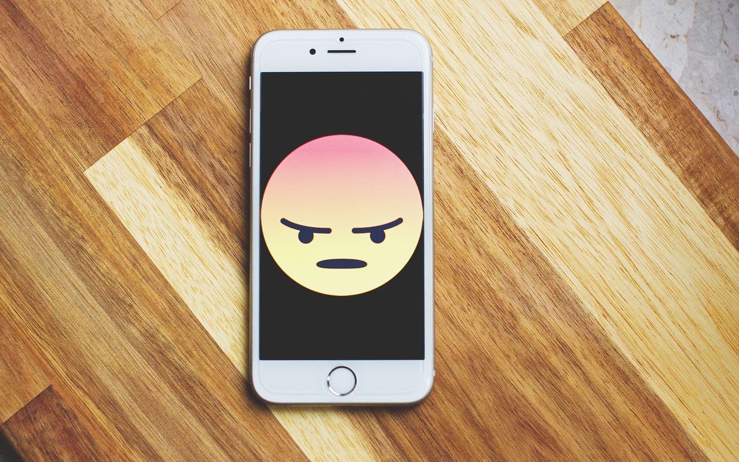 Smartphone mit wütendem Emoticon auf dem Display liegt auf einem Holztisch