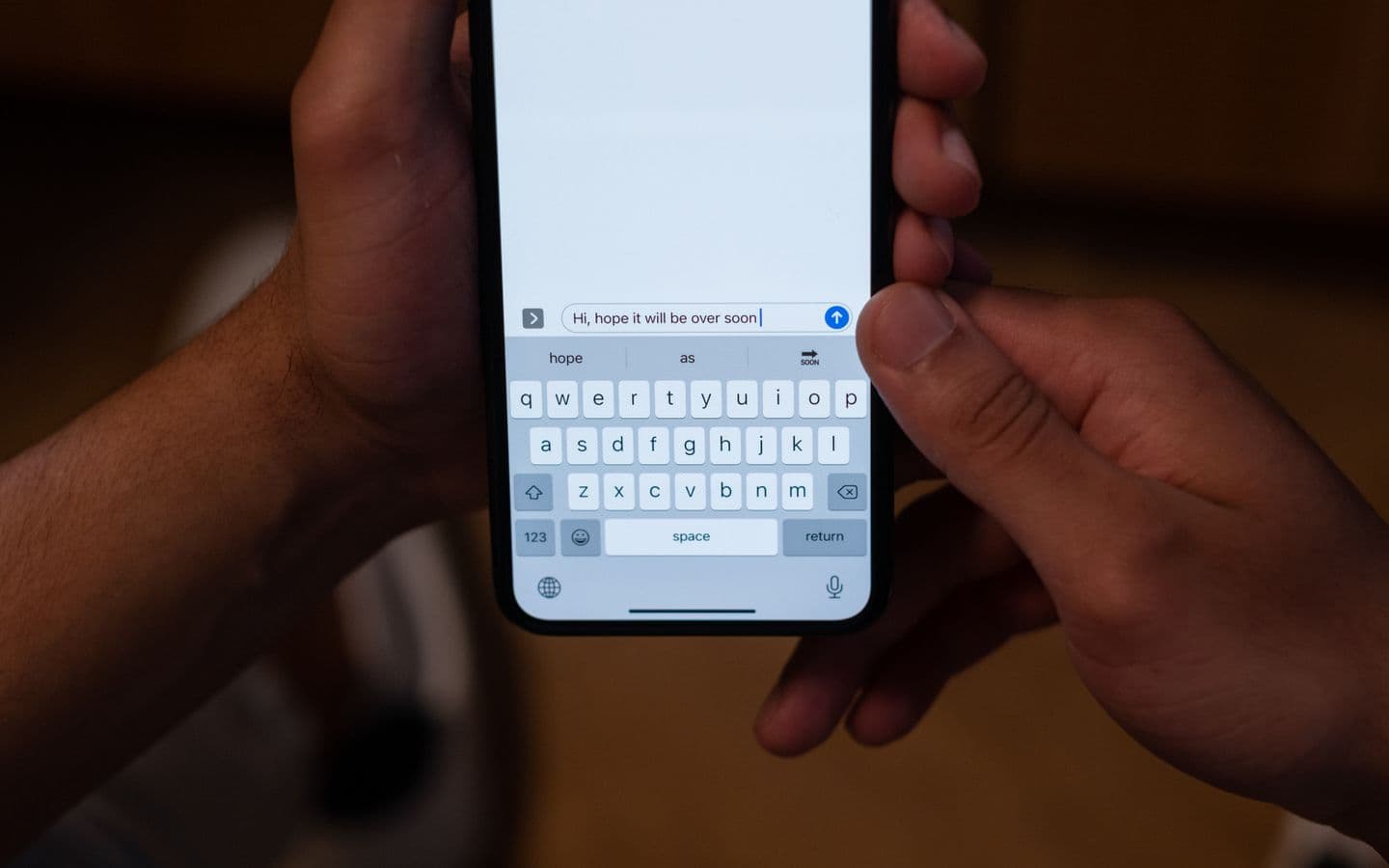 Nahaufnahme von Händen, die drinnen auf einem Smartphone eine hoffnungsvolle Nachricht tippen