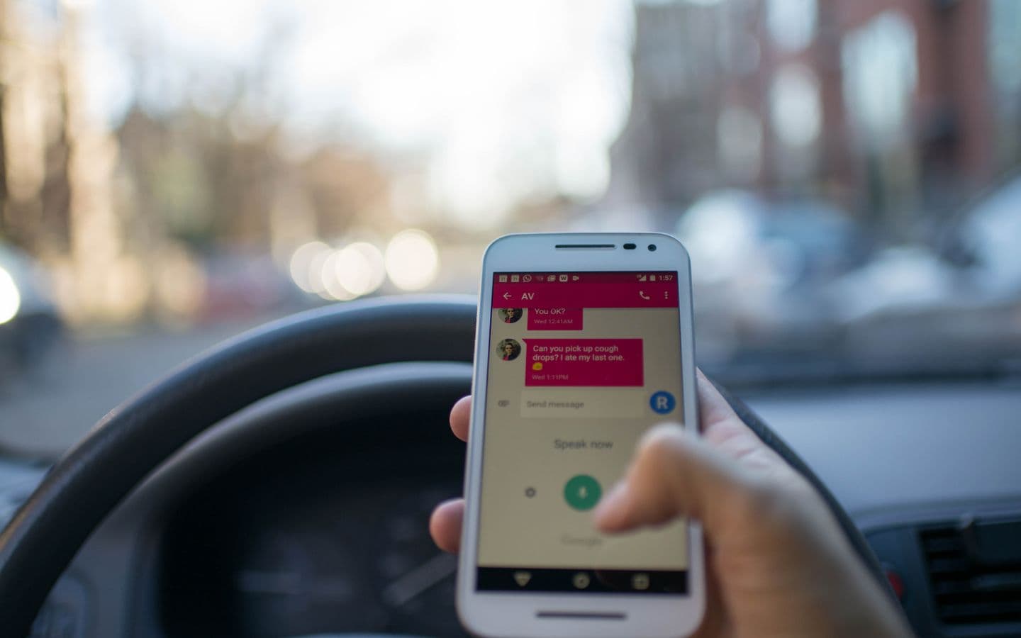 Person tippt am Steuer eines Autos in der Stadt eine Nachricht auf dem Smartphone