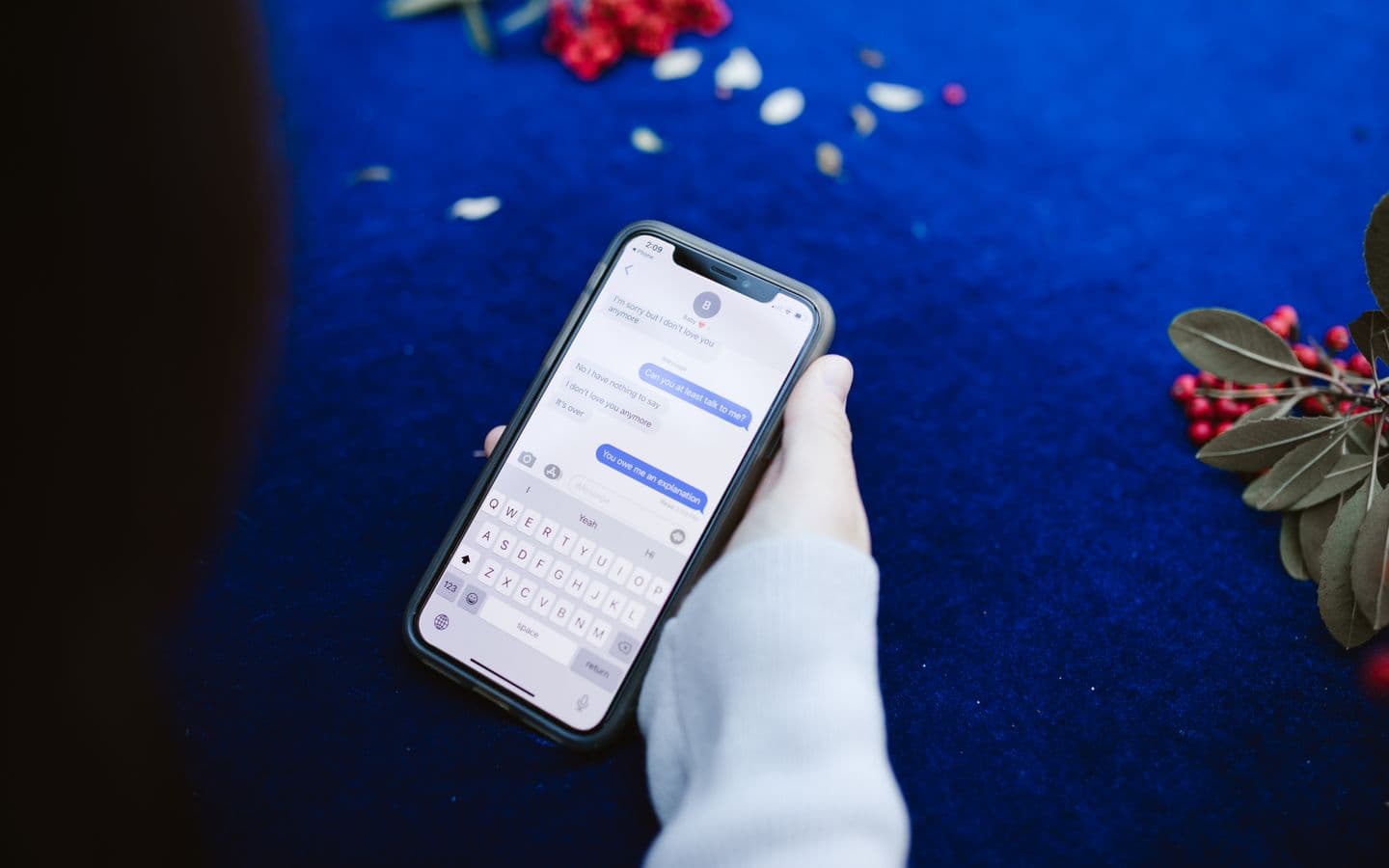 Person hält ein Smartphone mit Chatnachrichten über einer blauen Fläche mit Blumen
