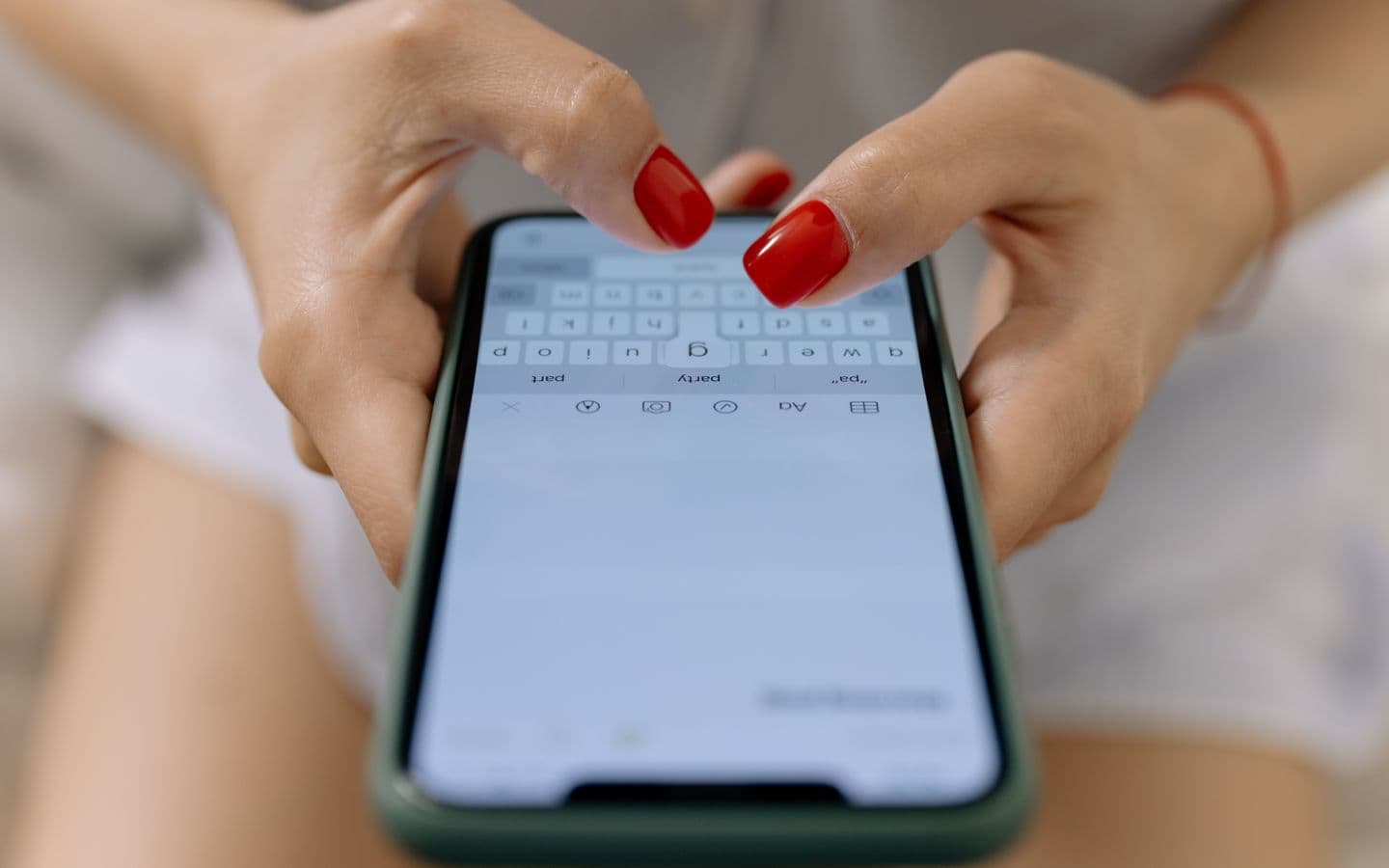 Nahaufnahme von Händen mit roten Nägeln, die auf einem Smartphone tippen